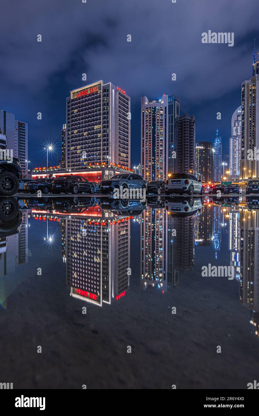 Skyscrapers of Dubai city skyline at blue hour. Reflections with parked cars and commercial buildings. Night mood of illuminated buildings in the UAE Stock Photo