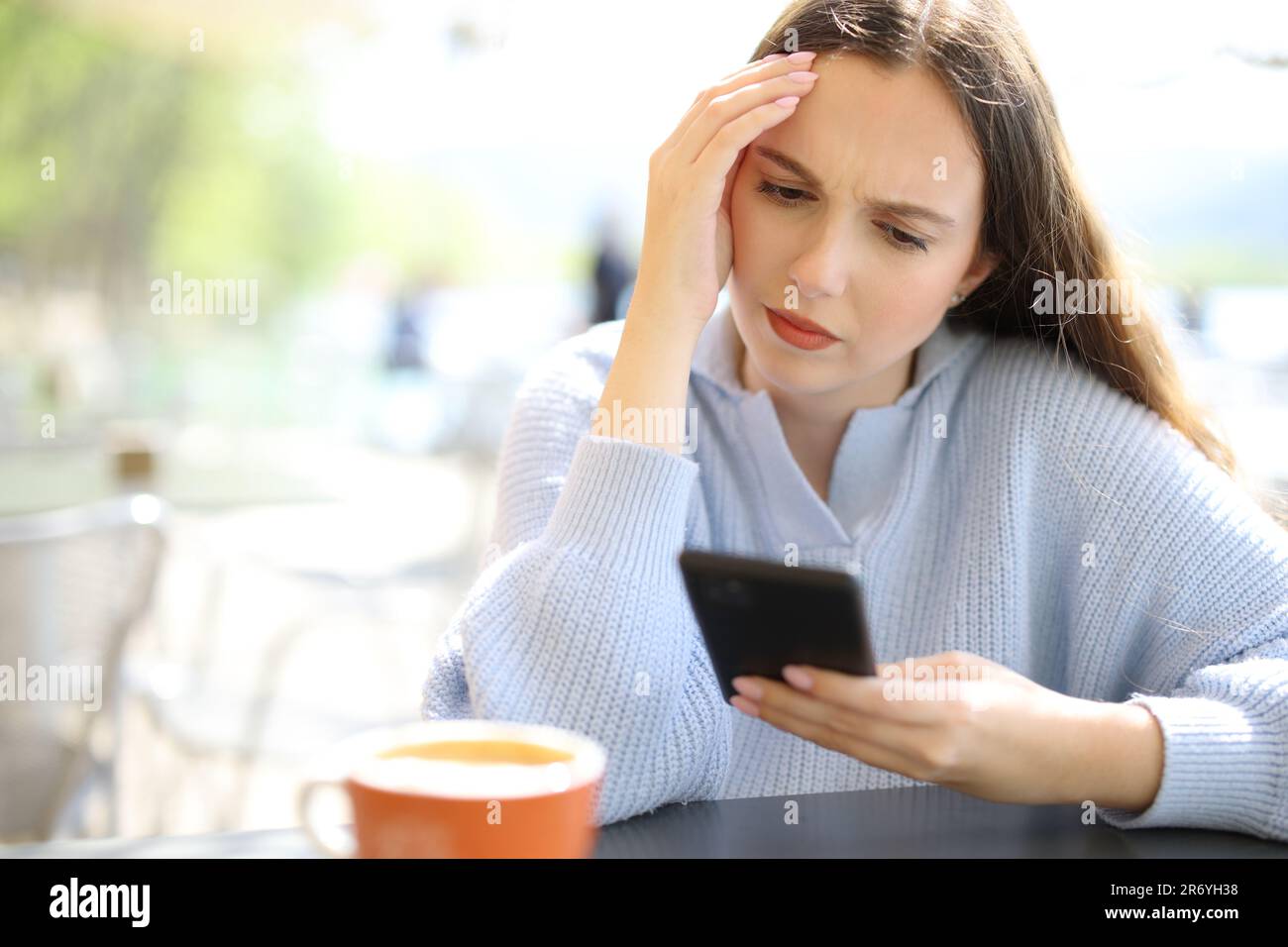 Worried woman checking phone sitting in a restaurant terrace a sunny day Stock Photo