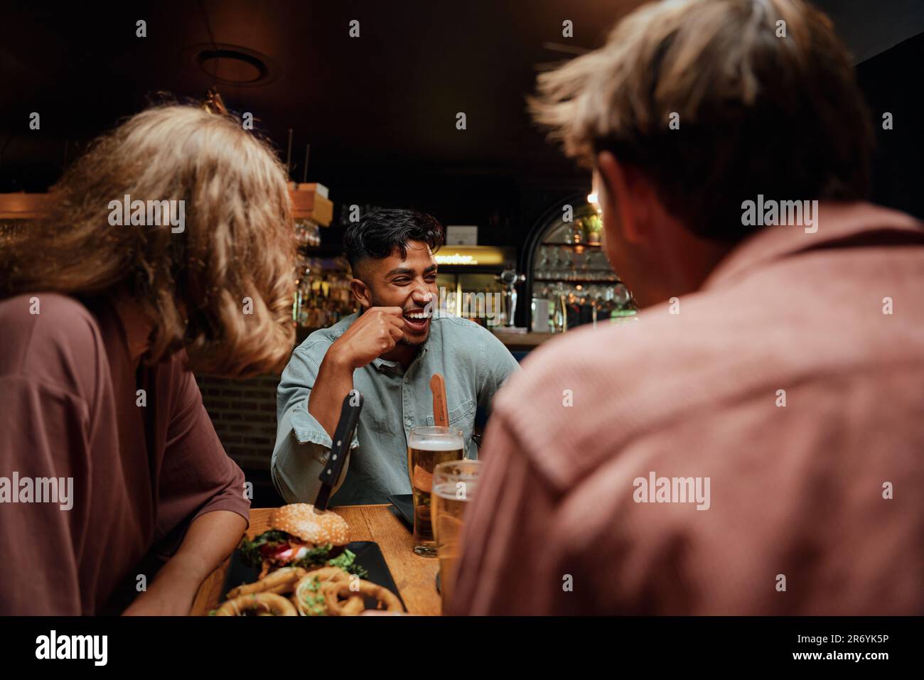 Young multiracial group of friends in casual clothing laughing during conversation over dinner Stock Photo