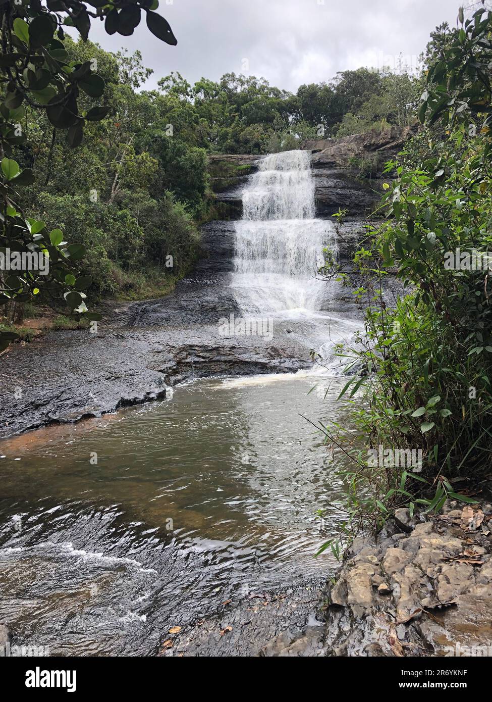 A waterfall cascading down the side of a lush green forest Stock Photo ...