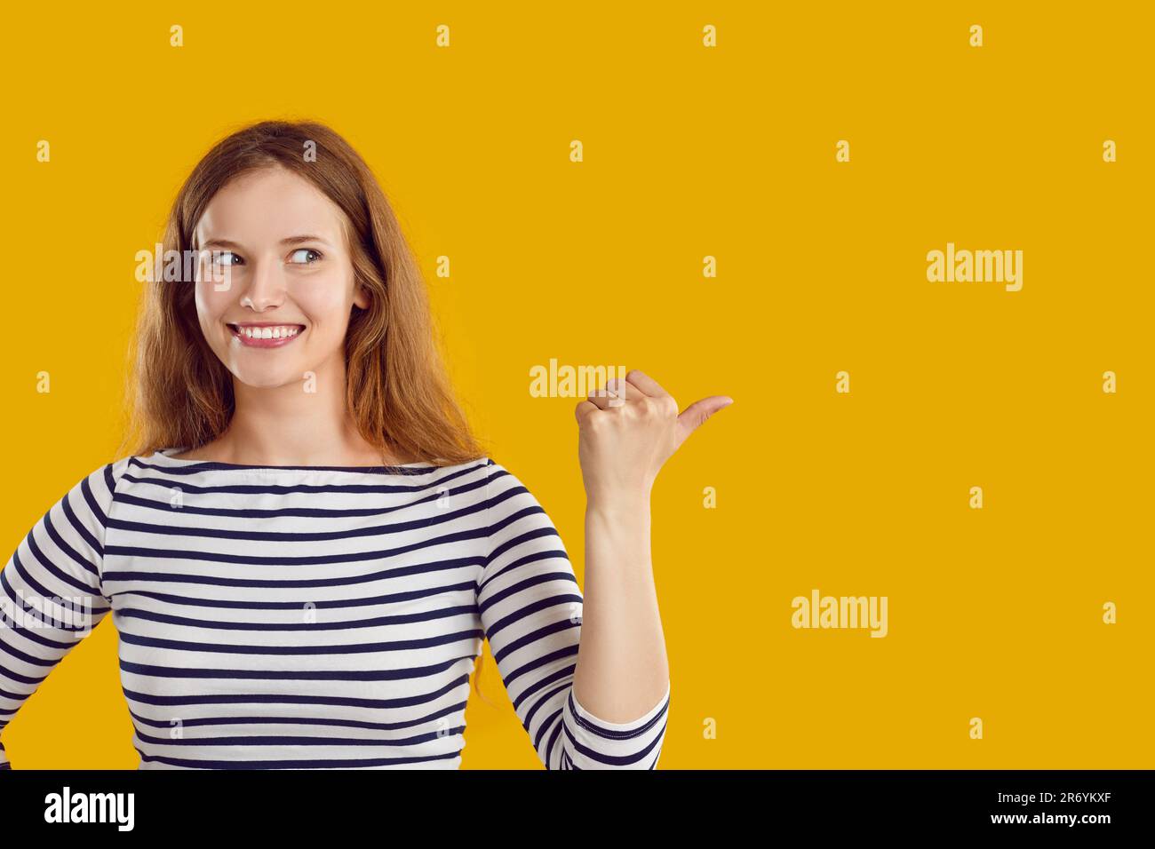 Happy beautiful young woman pointing to copy space side on yellow color background Stock Photo