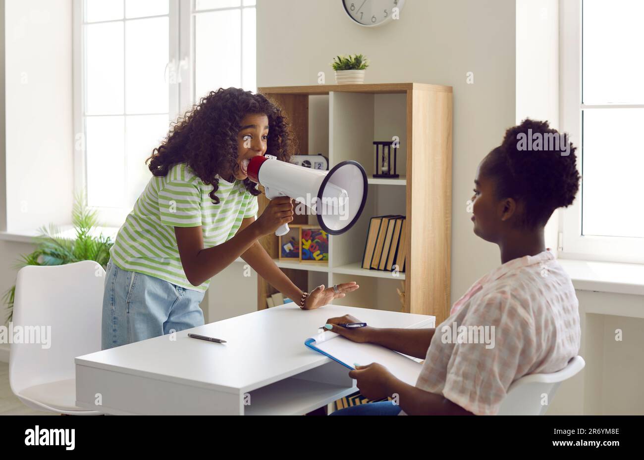 Stressed problem child seeking attention and screaming at psychologist through megaphone Stock Photo