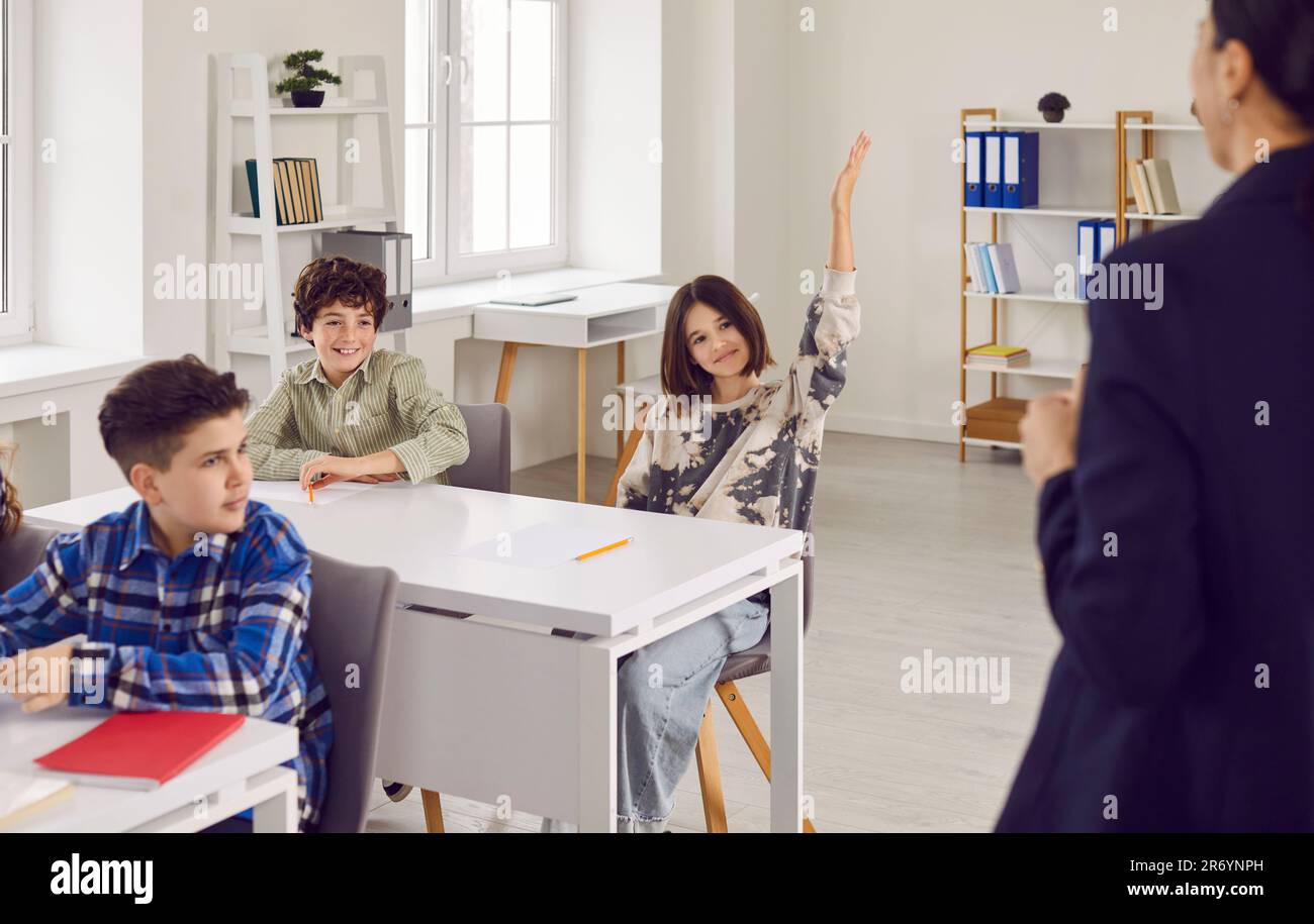 Schoolgirl sitting at the desk raising her hand up ready to answer in ...