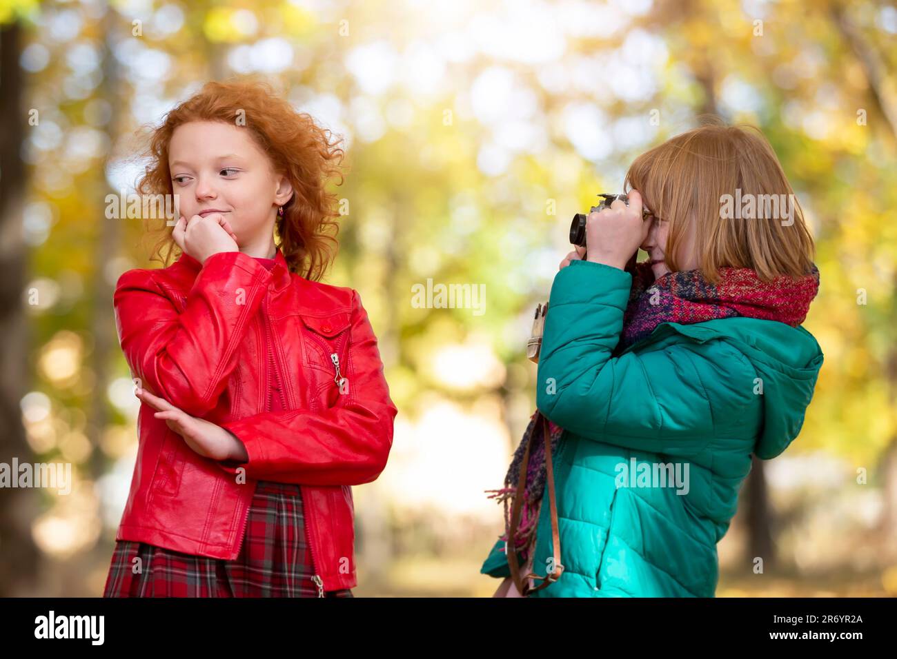 Two red-haired girls girlfriends photograph each other in the autumn park with a retro camera. Stock Photo