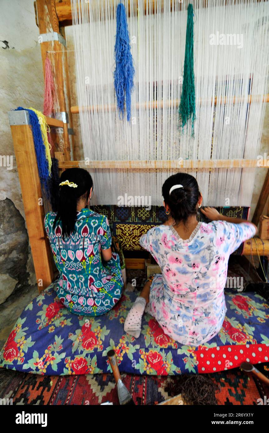 Uzbek women weaving a handmade traditional carpet in a small rug workshop in the old city of Bukhara, Uzbekistan Stock Photo