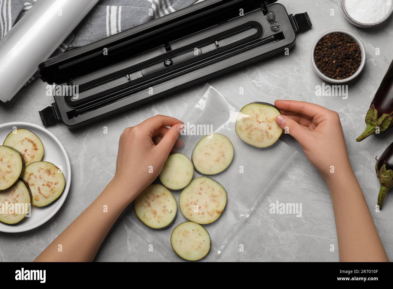 Woman packing cut eggplant into plastic bag using vacuum sealer on