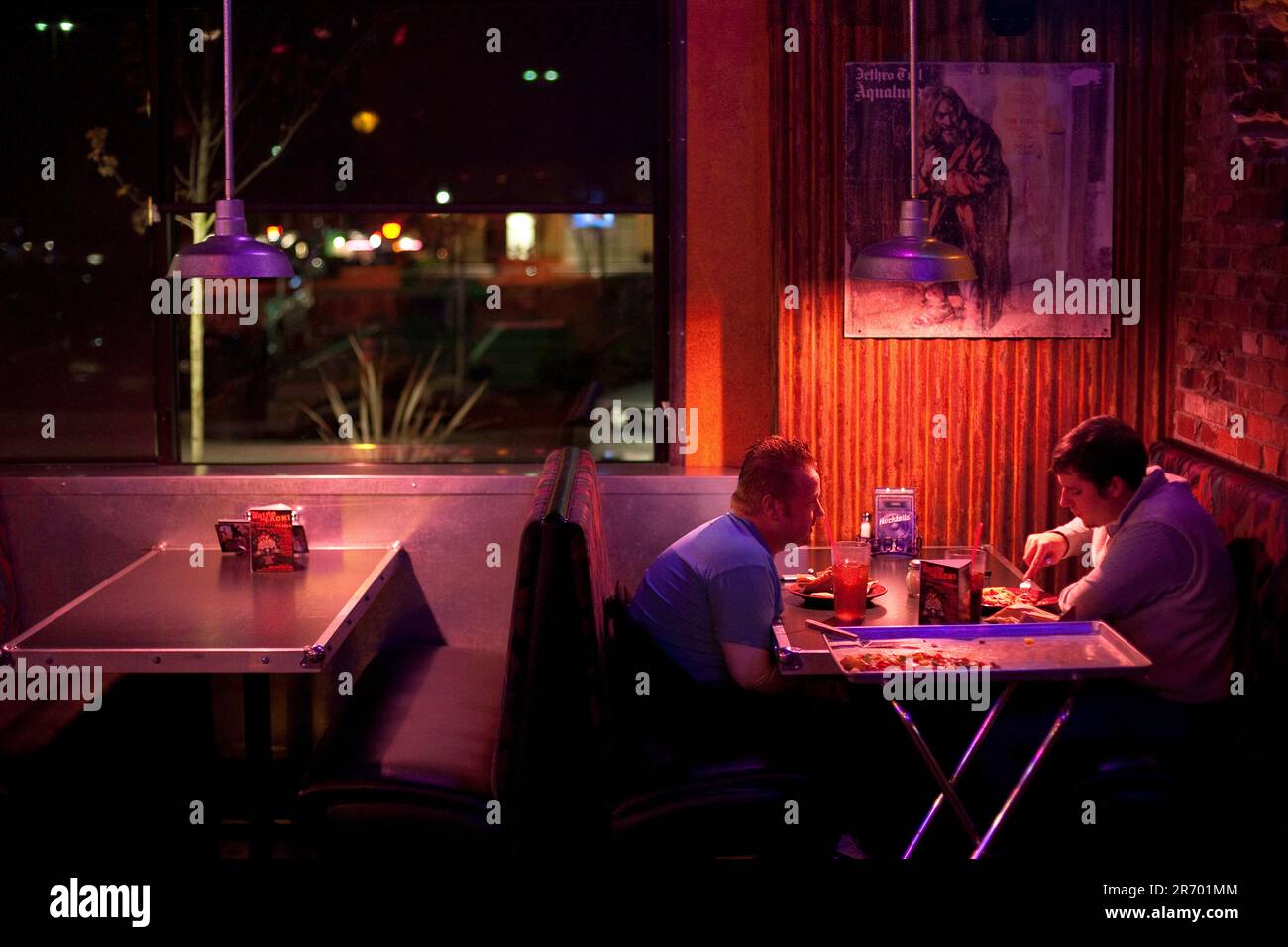 Two men sit at a table eating pizza at a dimly lit restaurant in Federal Way, Washington. Stock Photo