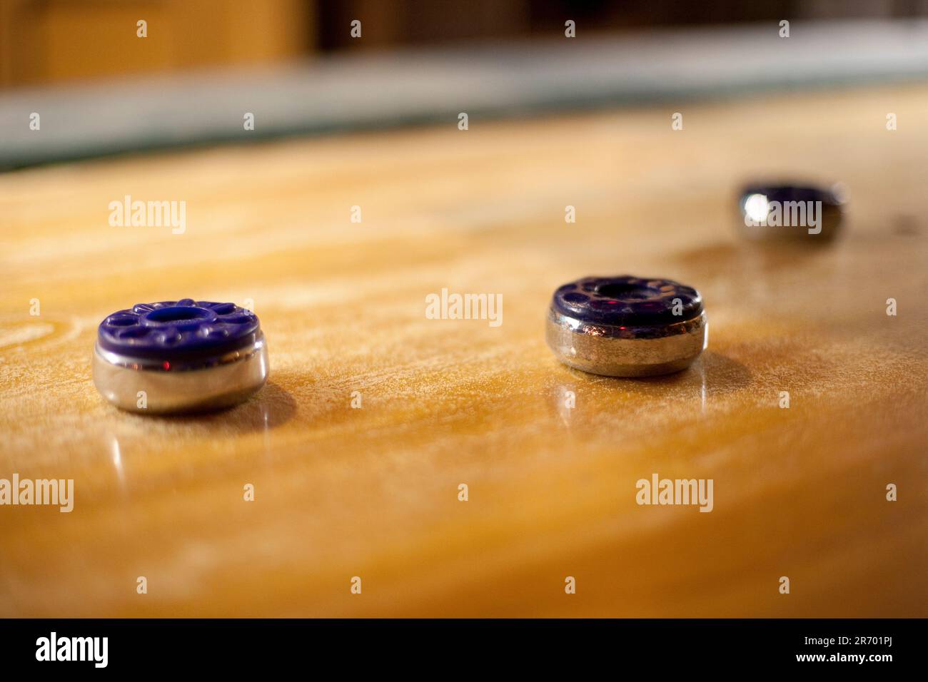 Three colorful discs rest atop a vintage wooden shuffleboard table at a