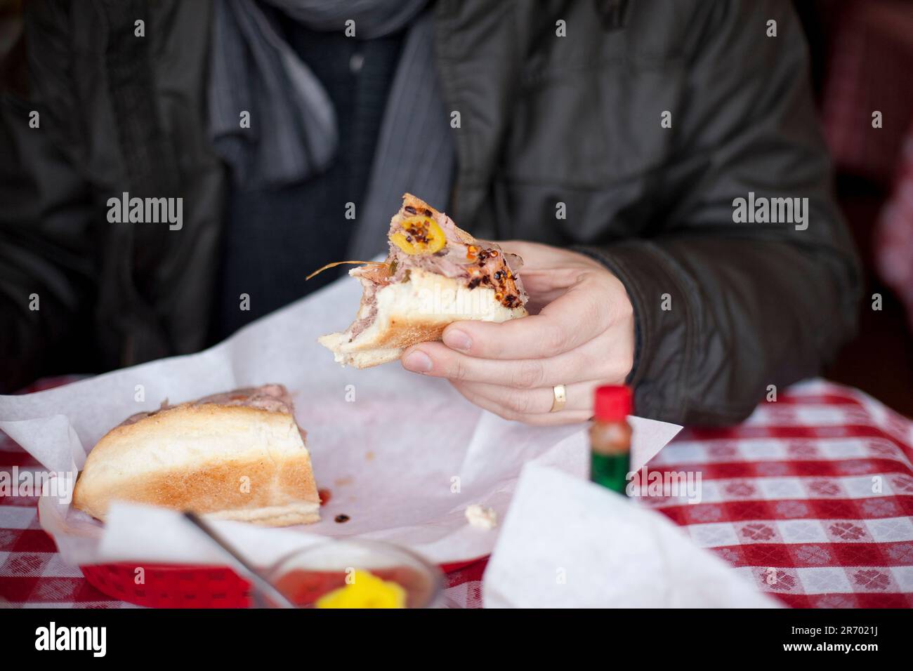 A man holds a half-eaten sandwich of thinly sliced Italian meats and hot peppers at a deli in Burien, Washington. Stock Photo