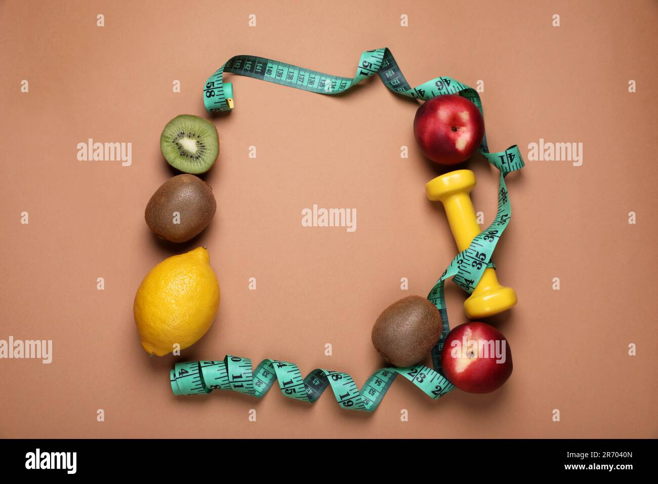 Frame of measuring tape, dumbbell and fresh fruits on light brown ...