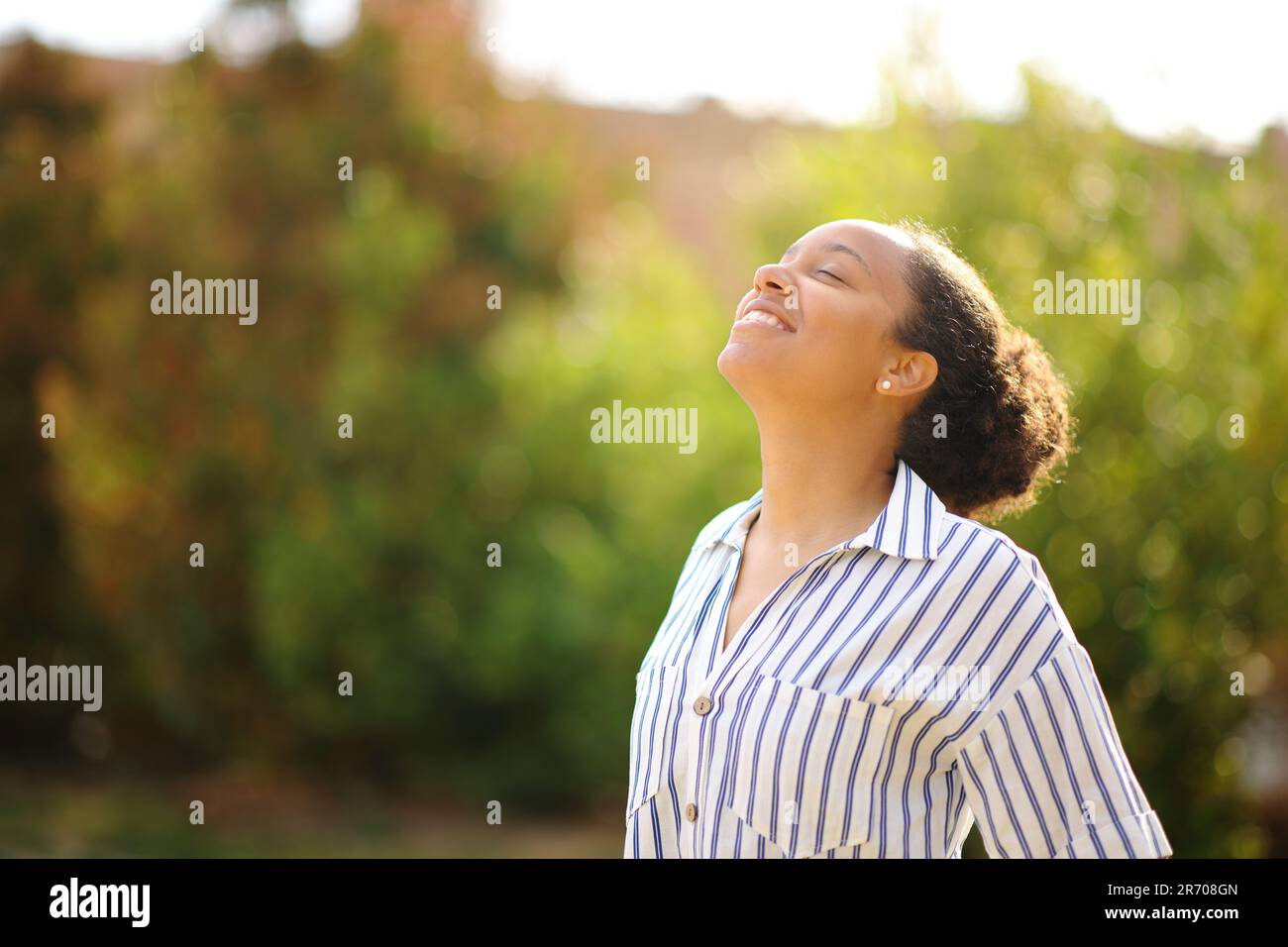 Happy black woman breathing fresh air standing in a park Stock Photo