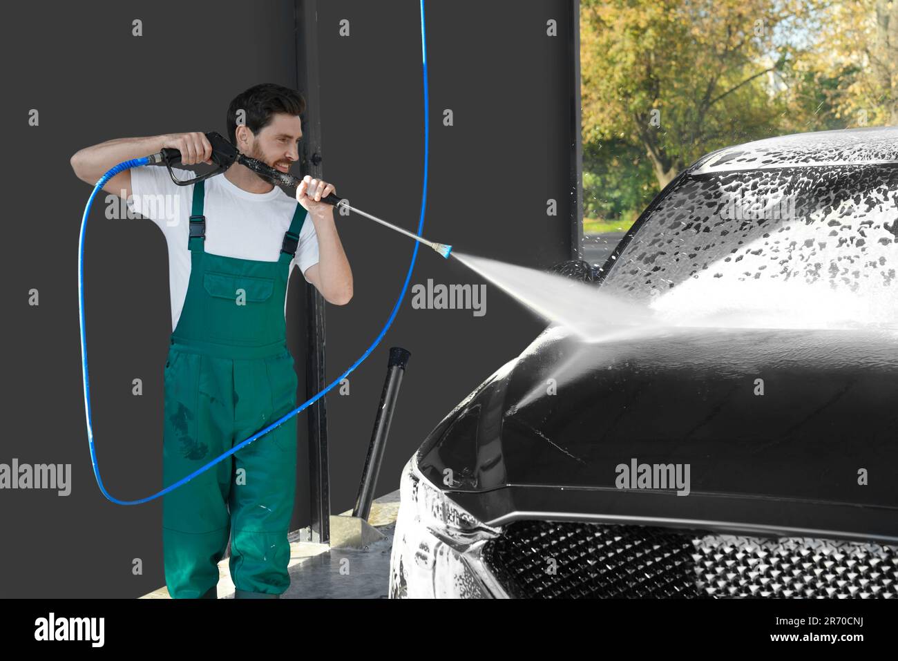 Worker washing auto with high pressure water jet at outdoor car wash
