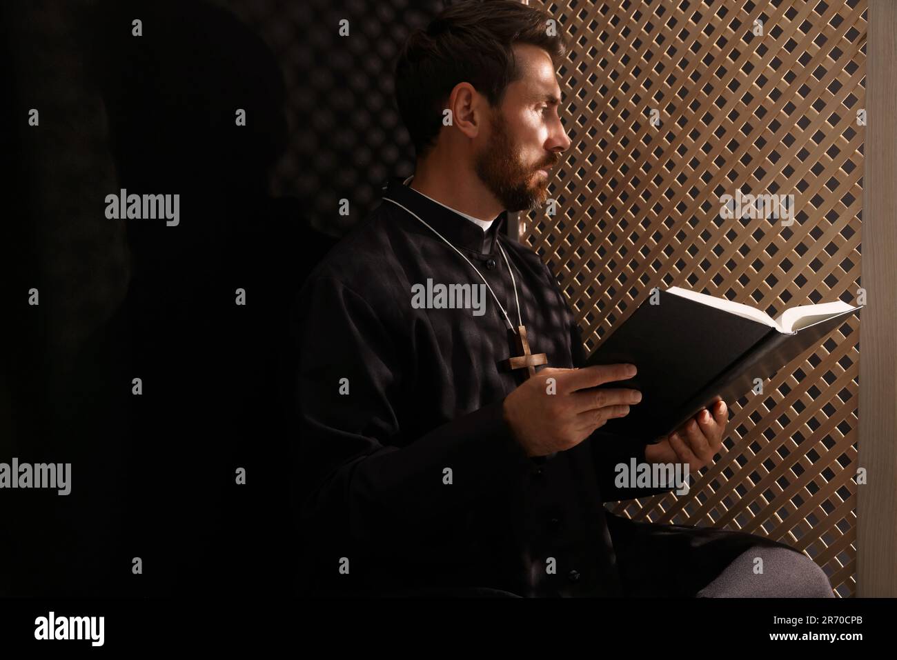 Catholic priest in cassock reading Bible in confessional booth Stock ...