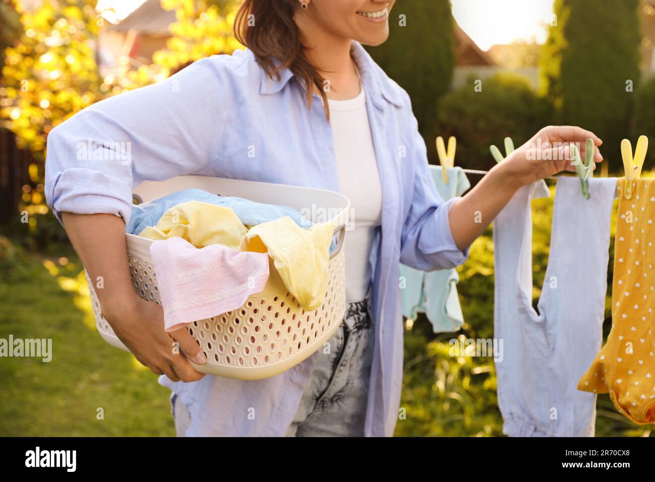 Smiling woman hanging baby clothes with clothespins on washing line for