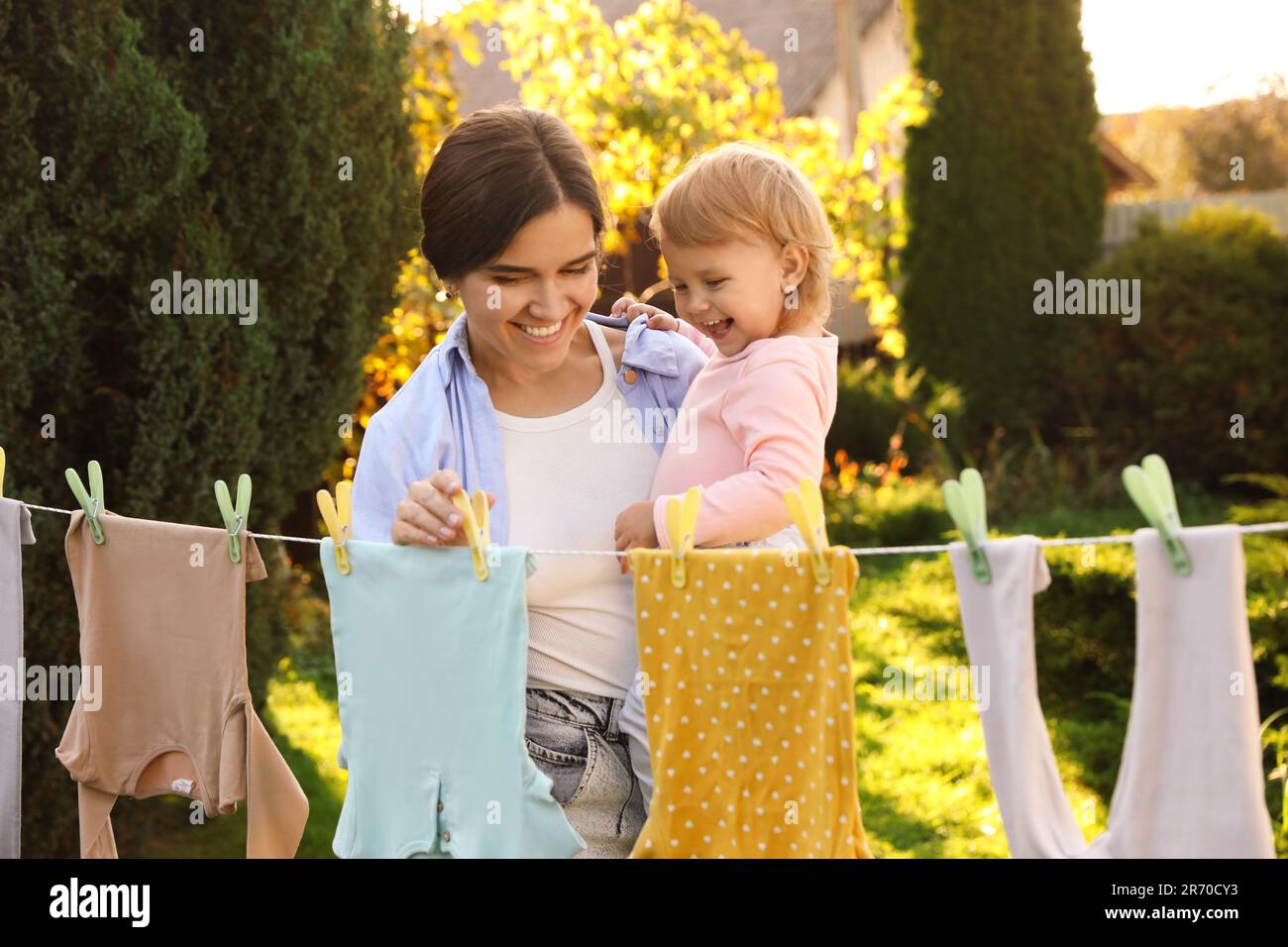Mother and daughter hanging clothes with clothespins on washing line for drying in backyard Stock Photo