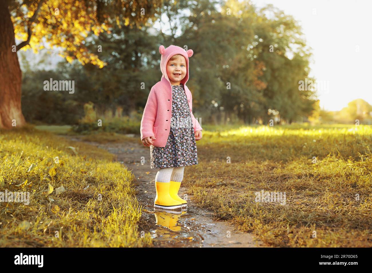 Little girl wearing rubber boots standing in puddle outdoors, space for ...