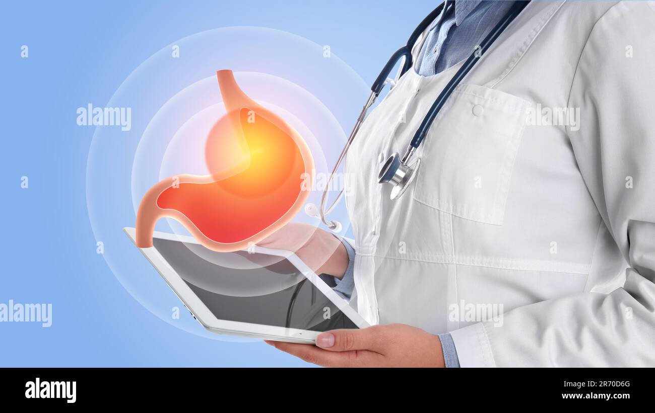 Treatment of heartburn and other gastrointestinal diseases. Doctor using tablet on light blue background, closeup. Stomach illustration over device Stock Photo