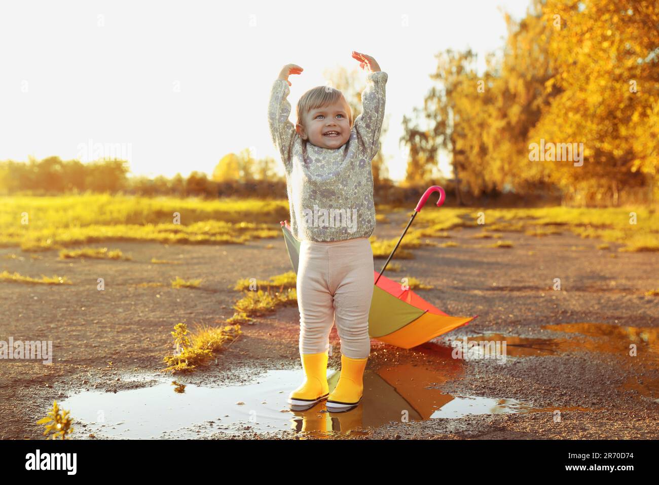 Little girl wearing rubber boots standing in puddle outdoors, space for ...