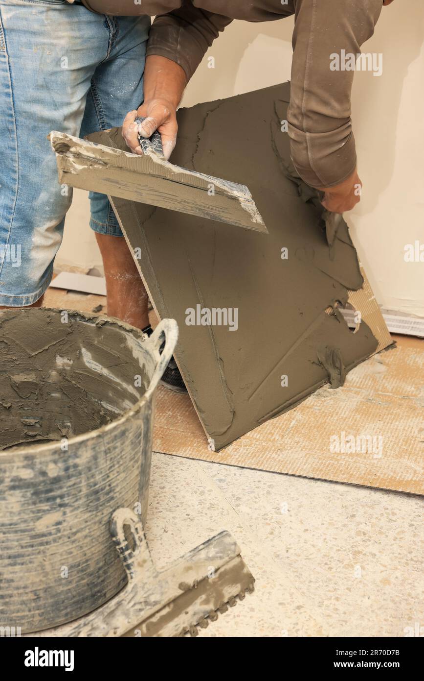 Worker spreading adhesive mix over tile with spatula, closeup Stock Photo