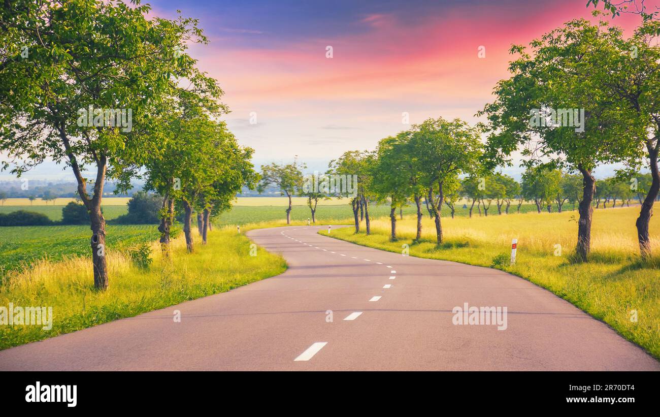 as the sun sets, the road leads through a beautiful countryside. journey continues promising a beautiful scene at every turn Stock Photo