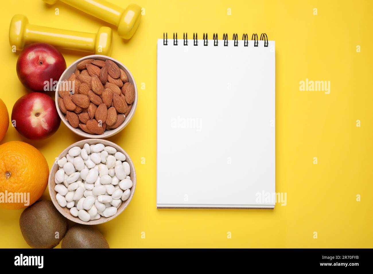 Notebook, fresh fruits and almonds on yellow background, flat lay. Low