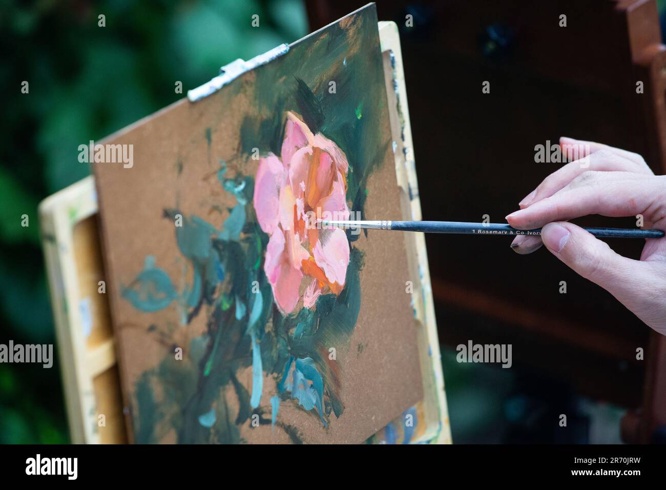 A painter hand holding a brush to paint a flower. Stock Photo