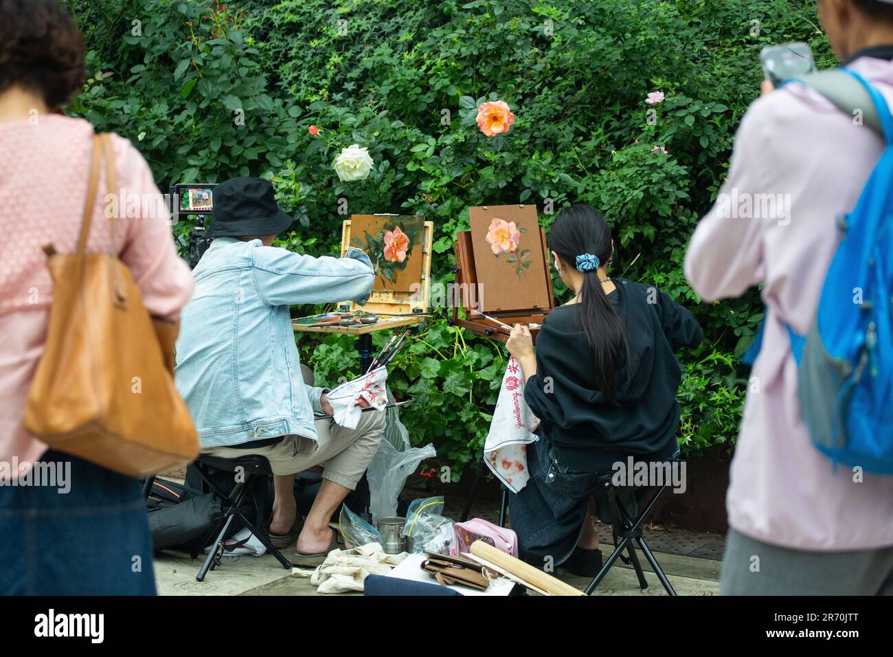 People gather behind the painters to check out their nature painting art work. Stock Photo