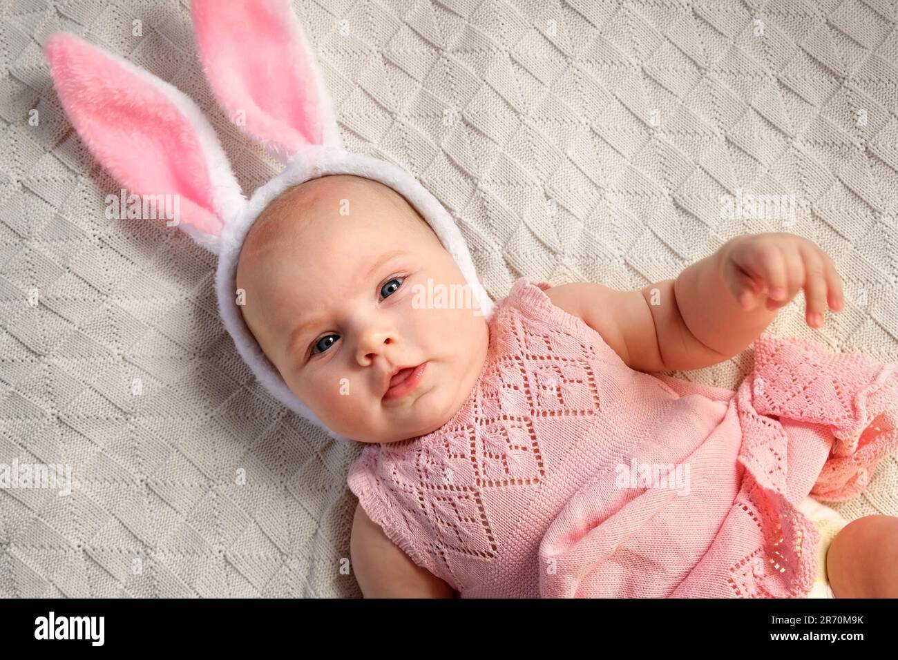 Funny little Child is wearing Bunny Ears on Cozy Background. Happy Easter. Baby Girl in pink Dress and Headband with Ears is lying on a Bed. Cute Newb Stock Photo Alamy