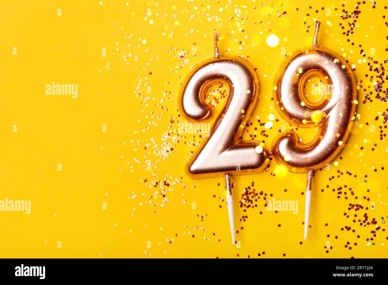 29 years celebration. Greeting banner. Gold candles in the form of number twenty nine on yellow background with confetti. Stock Photo
