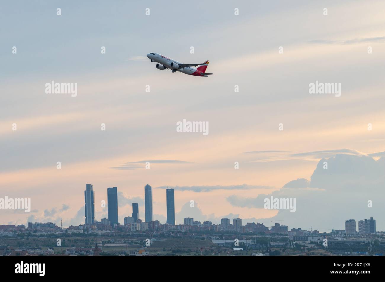An Iberia comercial flight flies over the skyscrapers of Madrid's skyline, known as the 'Four Towers Business Area', after departing from Adolfo Suare Stock Photo