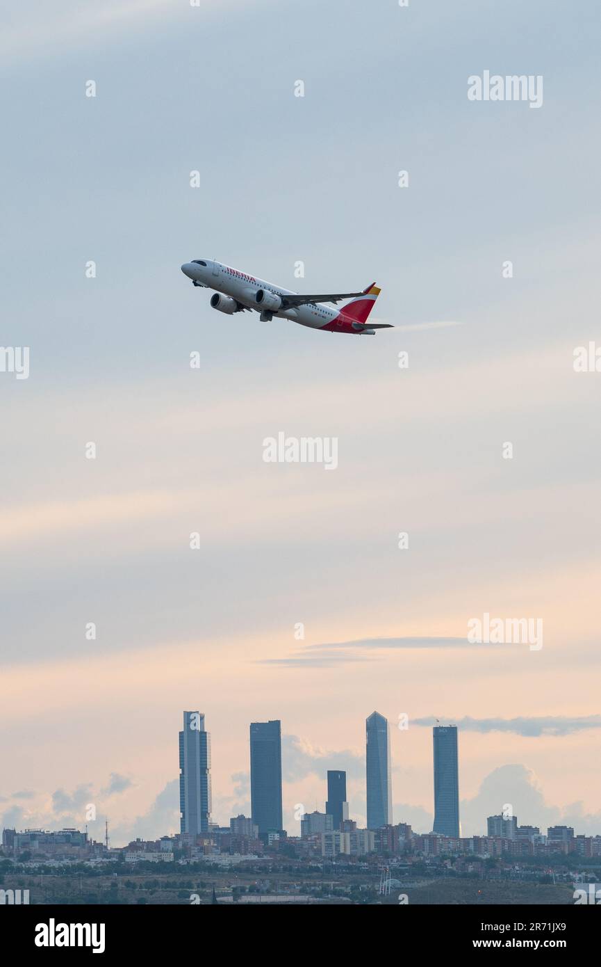 An Iberia comercial flight flies over the skyscrapers of Madrid's skyline, known as the 'Four Towers Business Area', after departing from Adolfo Suare Stock Photo