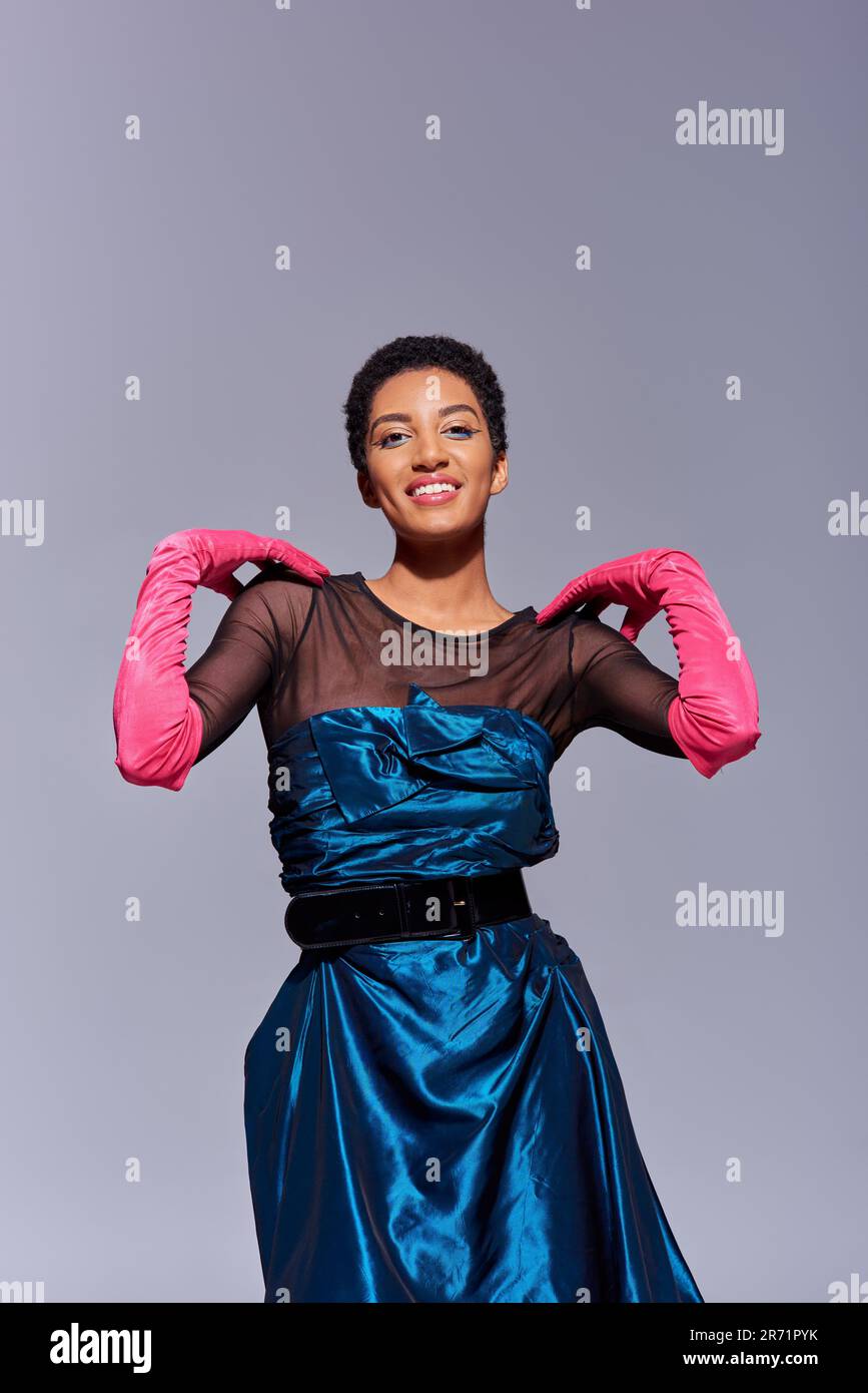 Positive african american woman in cocktail dress and pink gloves touching  shoulders and looking at camera isolated on grey, modern generation z fashi  Stock Photo - Alamy