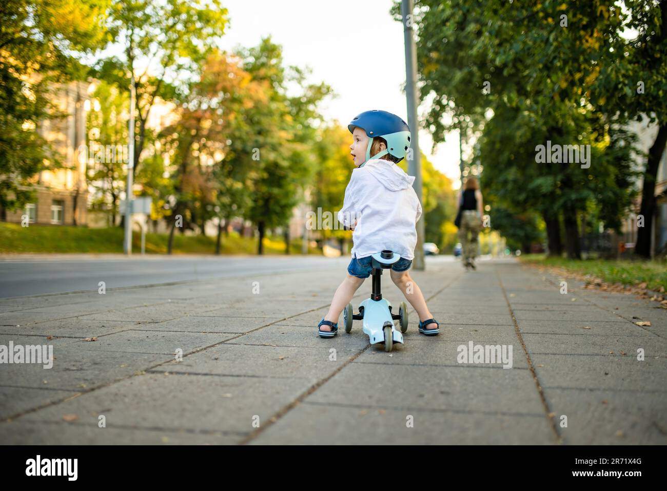 Funny toddler boy riding a baby scooter outdoors on summer day. Kid