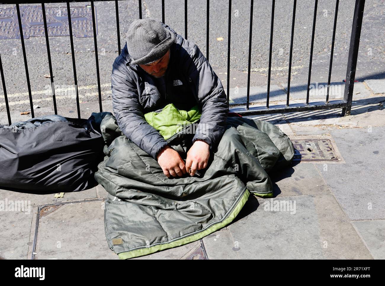 England, London, Trafalgar Square, Homeless man sat on pavement against metal railings. Stock Photo