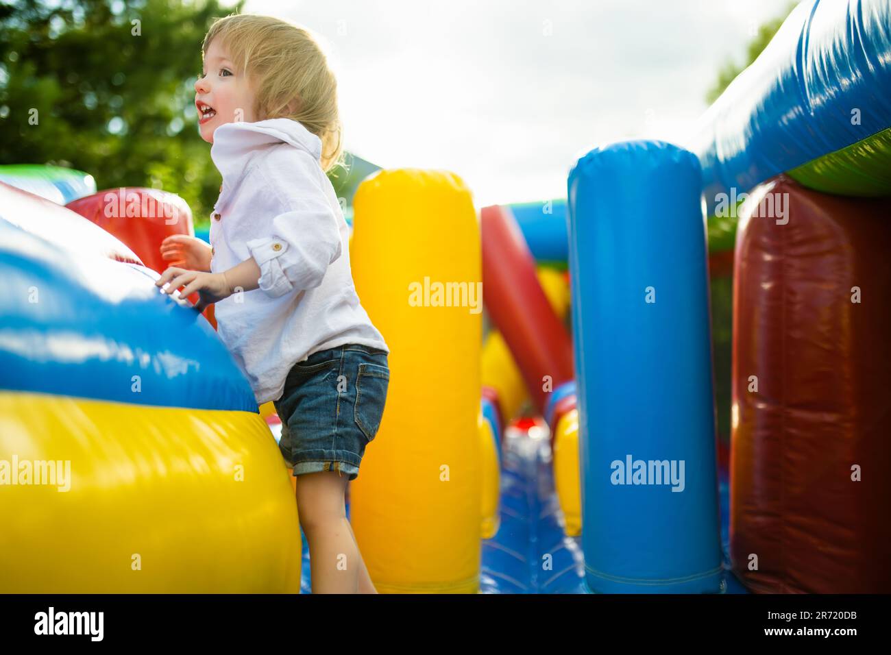 Cute toddler boy jumping on a inflatable bouncer in a backyard on warm and sunny summer day. Sports and exercises for children. Summer outdoor leisure Stock Photo