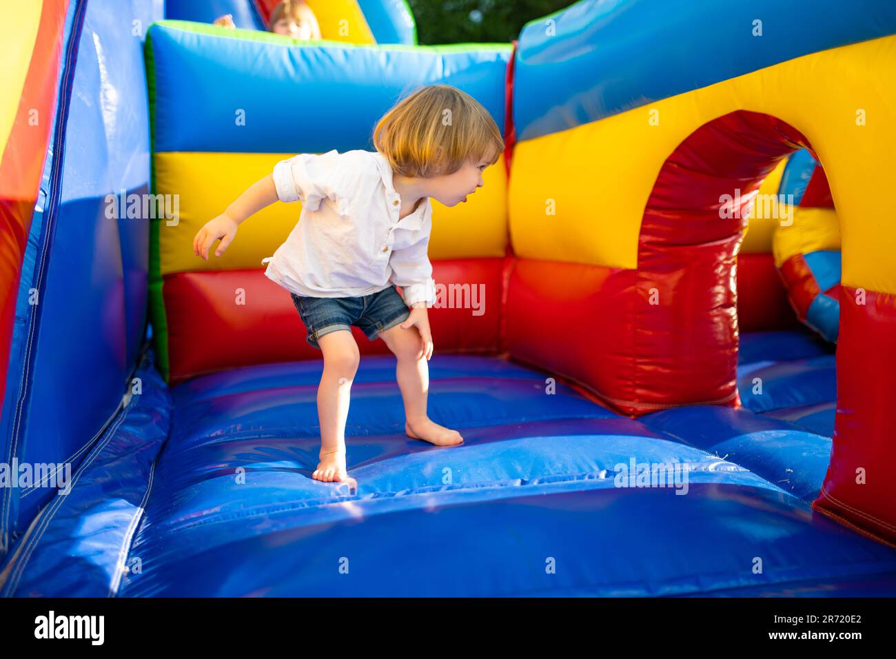 Cute toddler boy jumping on a inflatable bouncer in a backyard on warm and sunny summer day. Sports and exercises for children. Summer outdoor leisure Stock Photo