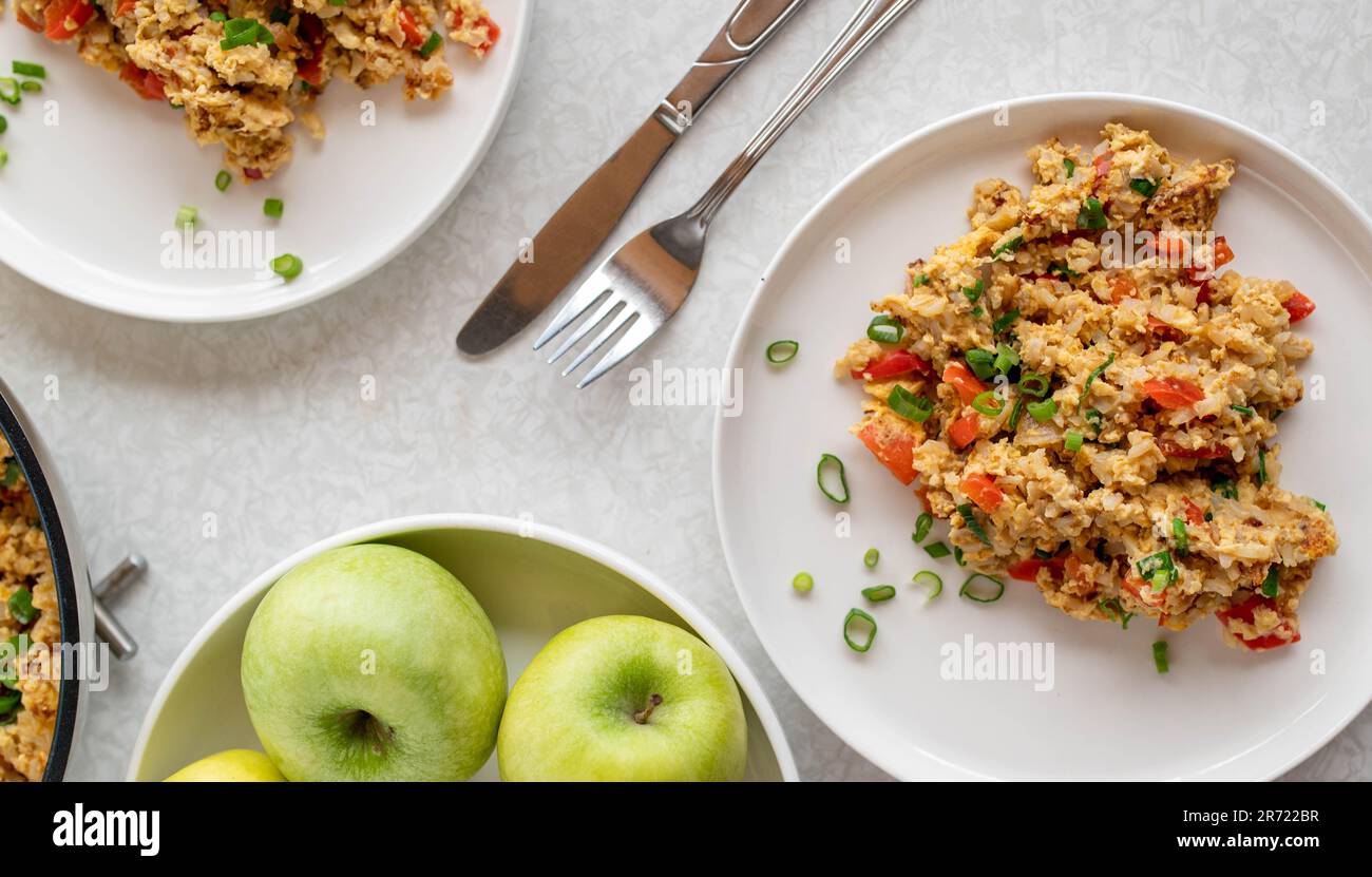 Fried brown rice with scrambeld eggs, tuna and vegetables on plates on white table background Stock Photo