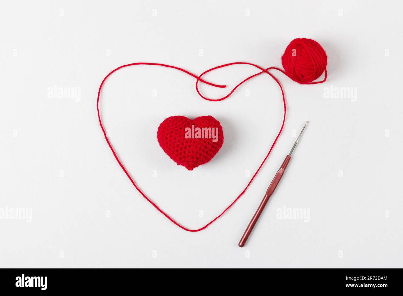 Crocheted red heart on a gray background and and a ball of thread with a hook. Symbol of love. Top view, flat lay Stock Photo