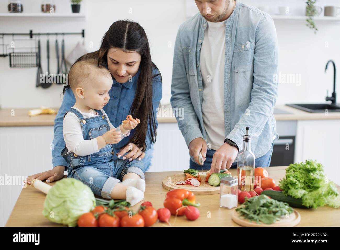 Sweet little girl in denim wear holding small slice of red vegetable