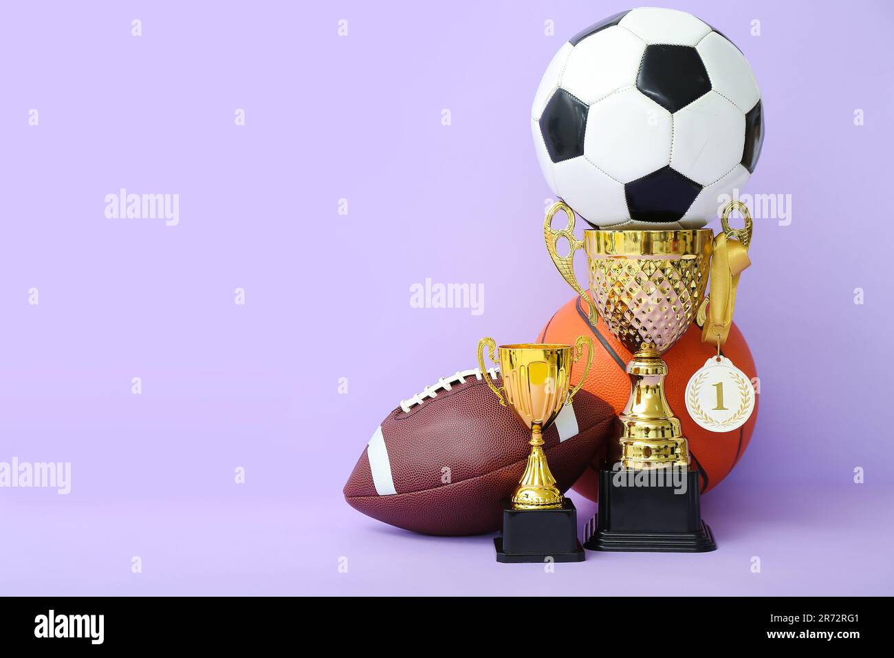 Gold cups with first place medal and balls on lilac background Stock Photo