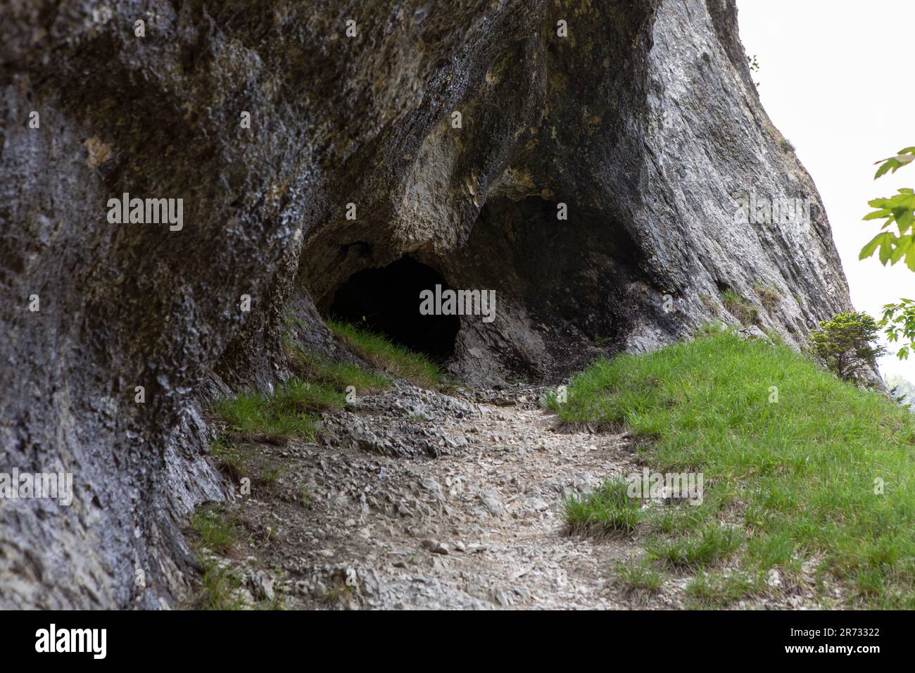 Path leading to entrance to the cave in Jura mountains. Black hollow in rock. Mountain tunnel hiking trail, cave enter of dark corridor, Gorges de Cou Stock Photo