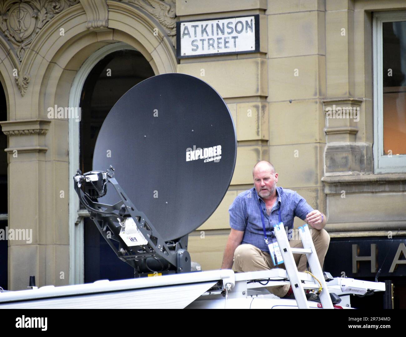 Manchester, UK. 12th June, 2023. A man sits on a satellite tv truck as fans wait as Manchester City Football Club gets ready to hold an open top bus victory parade in central Manchester, UK, to mark the achievement of winning the treble: the Premier League, the FA Cup, and the Champions League. On Saturday Man City beat Inter Milan in Istanbul to secure the Champions League win. The parade of open top buses went through Manchester city centre watched by large, enthusiastic crowds, despite a thunderstorm and heavy rain. Credit: Terry Waller/Alamy Live News Stock Photo