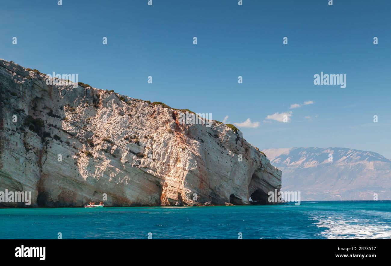 Blue caves, rocky coast of Zakynthos island with natural stone arches. Tourists on boats visit the popular natural landmark on a sunny summer day Stock Photo