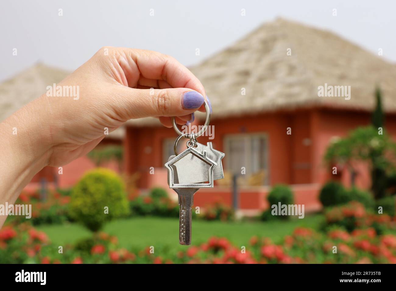Real estate agent, home keys in female hand on background of house with thatched roof. Buying or rental a villa, removal to tropical country Stock Photo