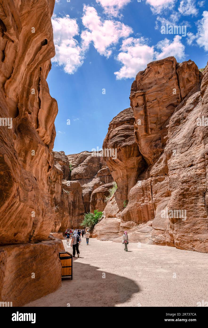 People walk in the Siq, the main entrance to Petra, Jordan. It is a dim, narrow gorge that ends to the Treasury. Stock Photo
