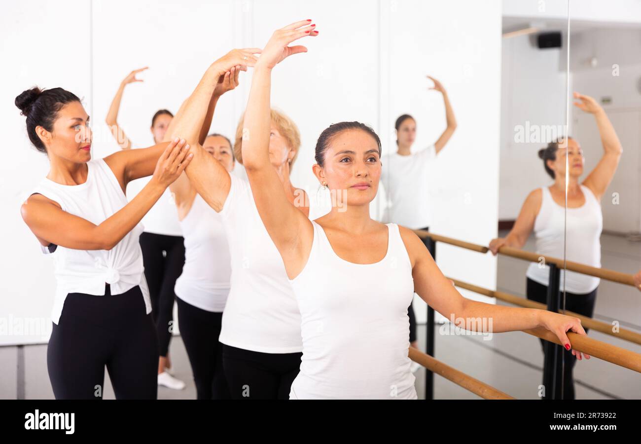Female ballet trainer teaching group of dancers near ballet barre in