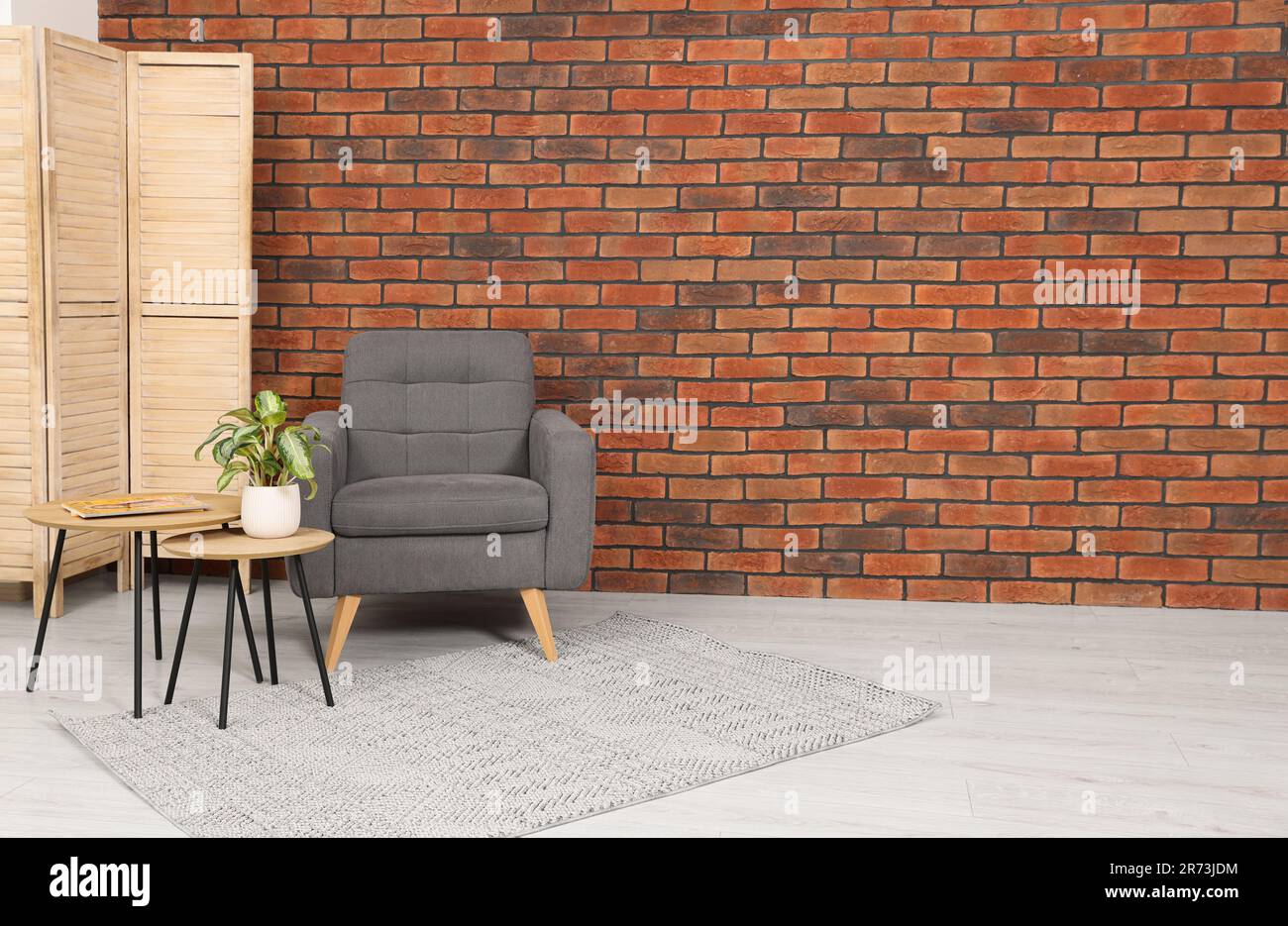Cosy armchair and potted plant on coffee table near brick wall in room ...