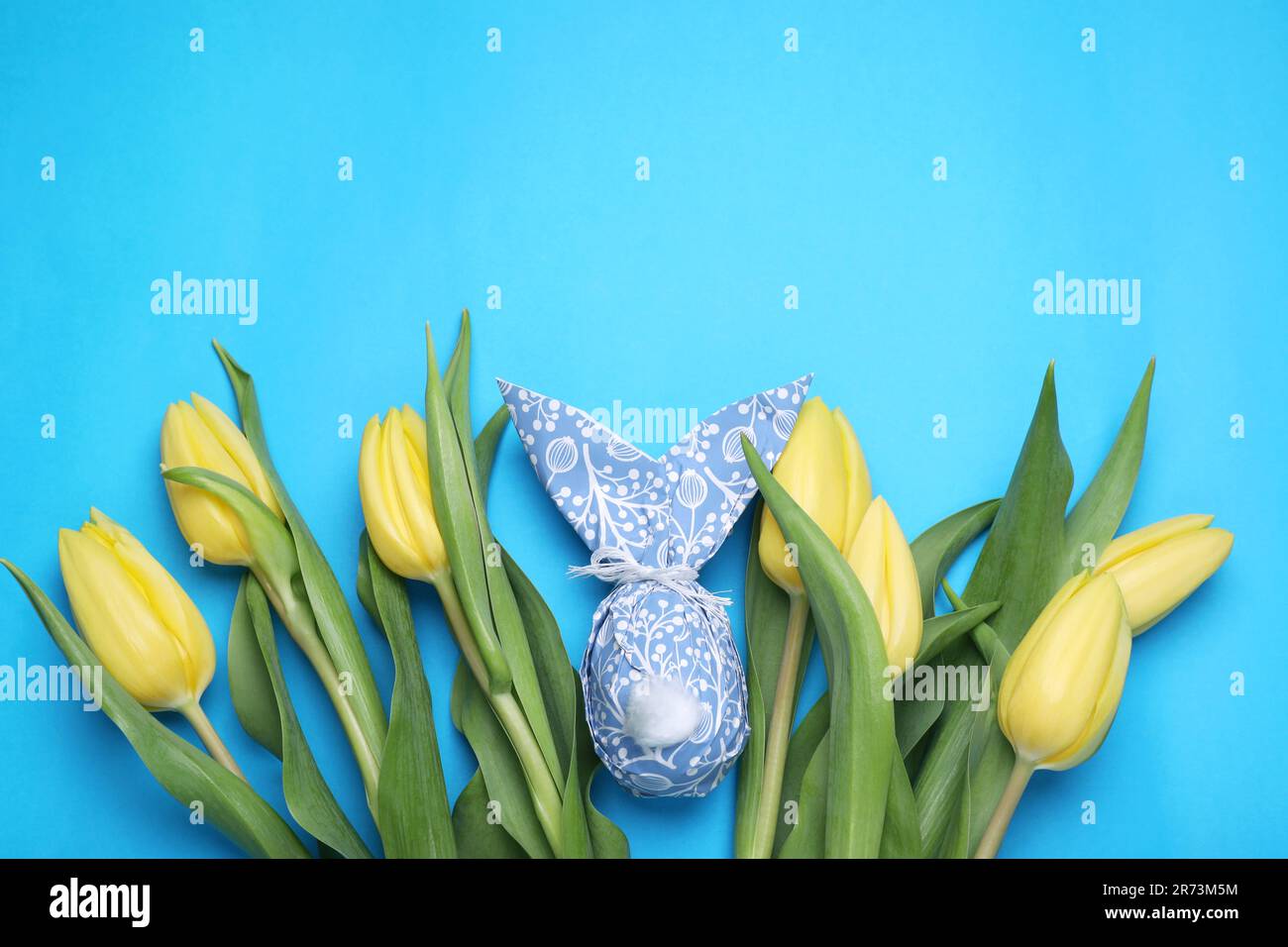 Easter bunny made of paper and egg among beautiful tulips on light blue ...