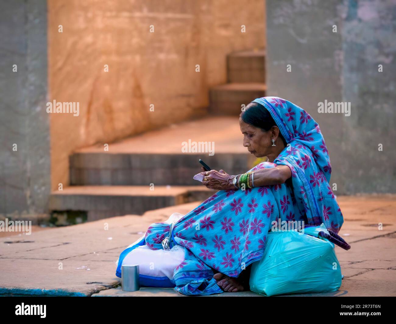 Varanasi, India - Nov 11, 2015. A senior Indian woman wearing a traditional sari and headscarf uses a cellphone while sitting outdoors. Stock Photo