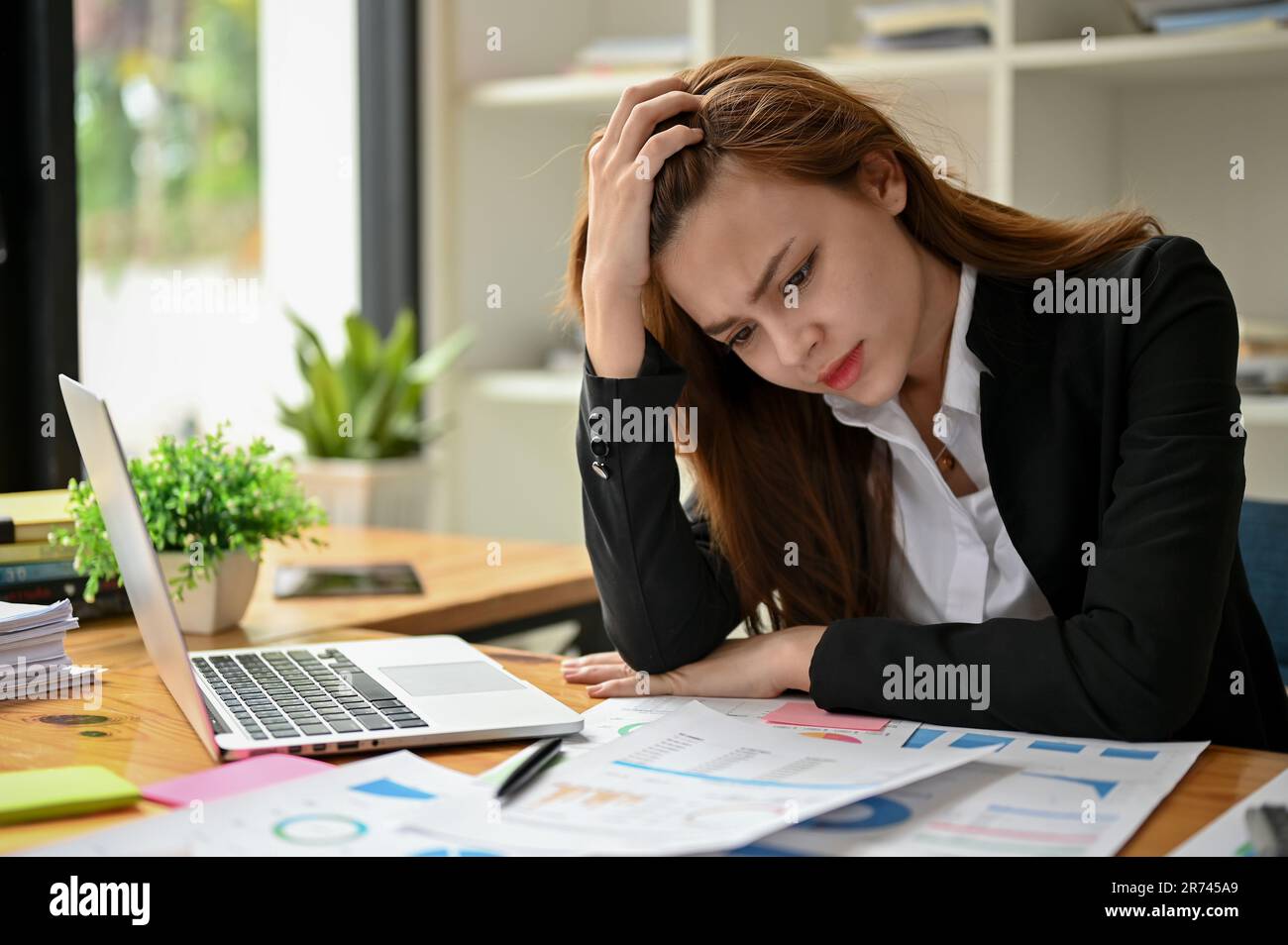 A stressed and frustrated Asian businesswoman feels dissatisfied and worried with her business financial plan, suffering from headaches and being over Stock Photo